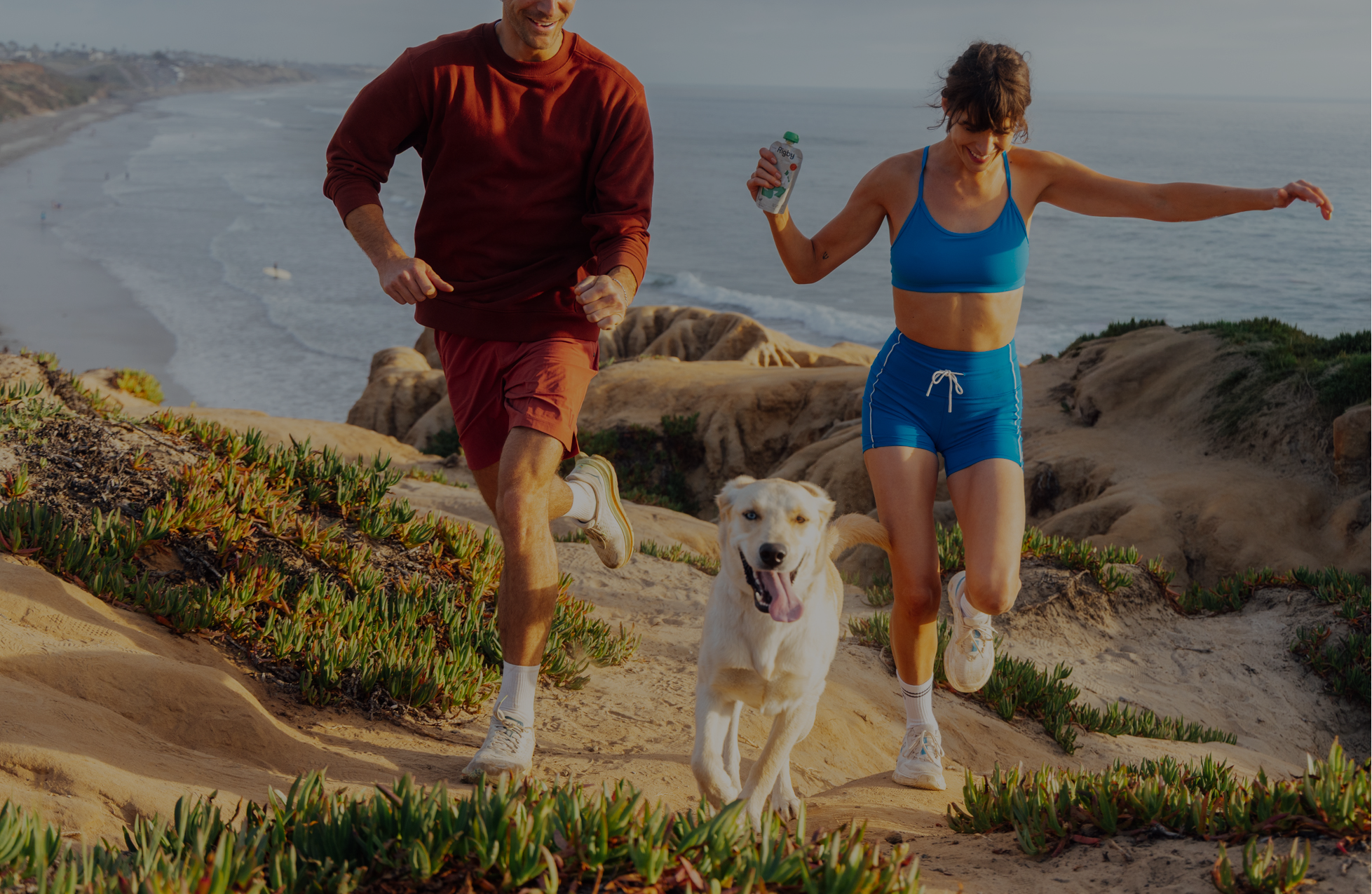 Two people running on a beach with a dog