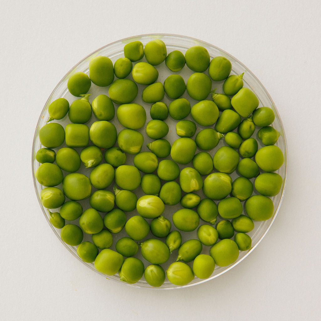 Fresh green peas in a glass dish, viewed from above.